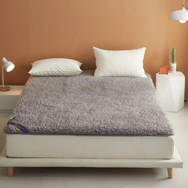 Modern bed with white frame, two white pillows, gray fluffy mattress topper, bedside tables, lamp, and cactus