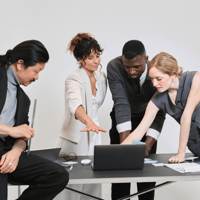 A diverse team of professionals collaborating around a laptop in a modern office setting, representing Wedaily Supplies Business Essentials