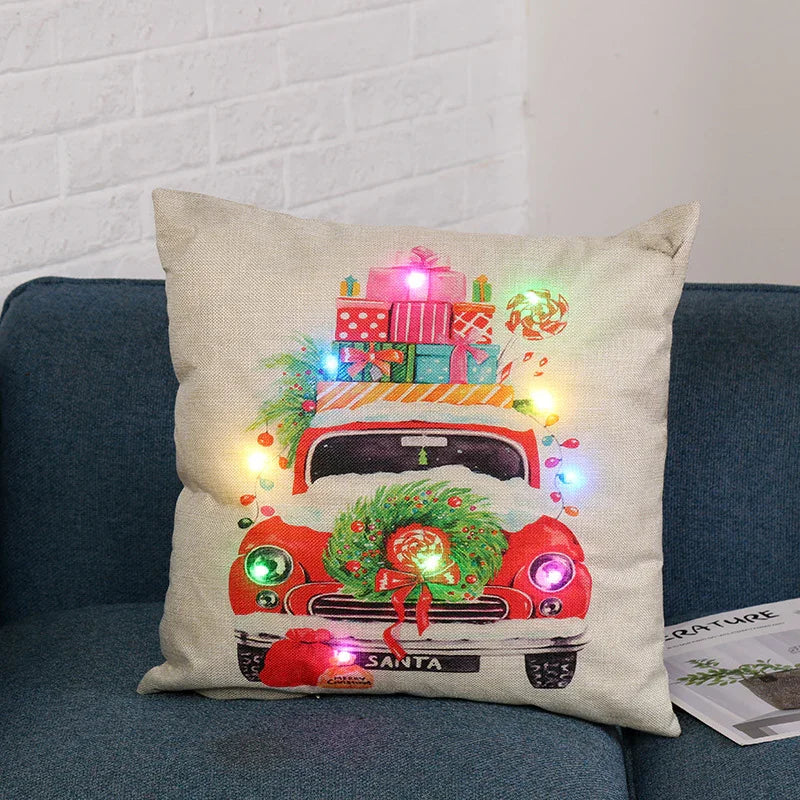 Beige decorative pillow with red vintage truck carrying Christmas presents and wreath, multicolor LED lights