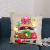 Beige decorative pillow with red vintage truck carrying Christmas presents and wreath, multicolor LED lights