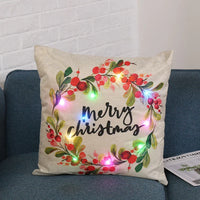 Beige Christmas pillow with colorful berry wreath and multicolor LED lights on a blue couch