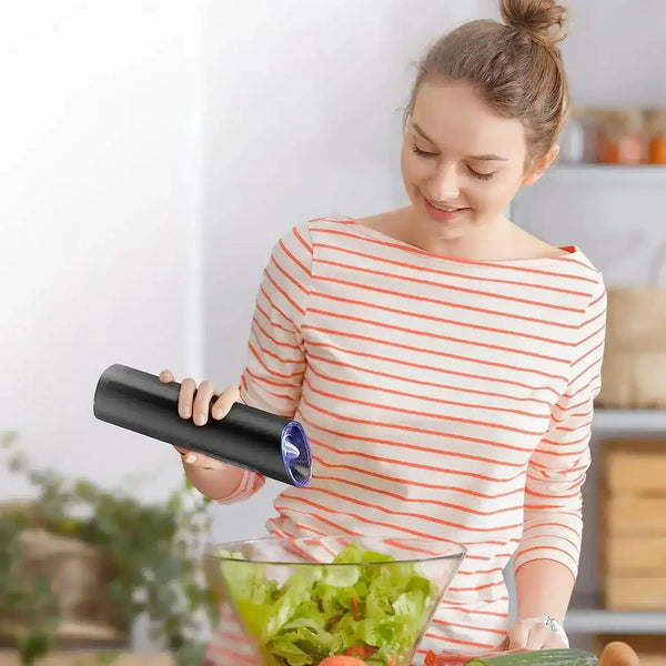 Woman using electric salt and pepper grinder to sprinkle seasoning on food