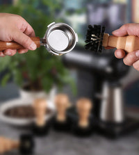 Hands demonstrating coffee machine cleaning brush removing grounds from espresso portafilter basket