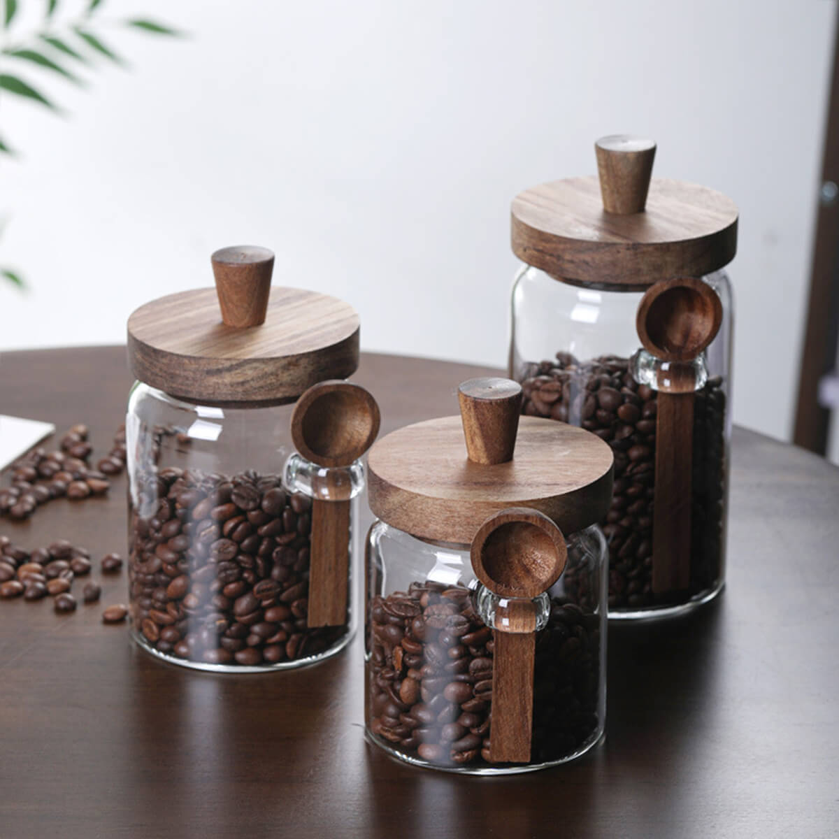 Three glass coffee jars with walnut lids and spoons in ascending sizes on table