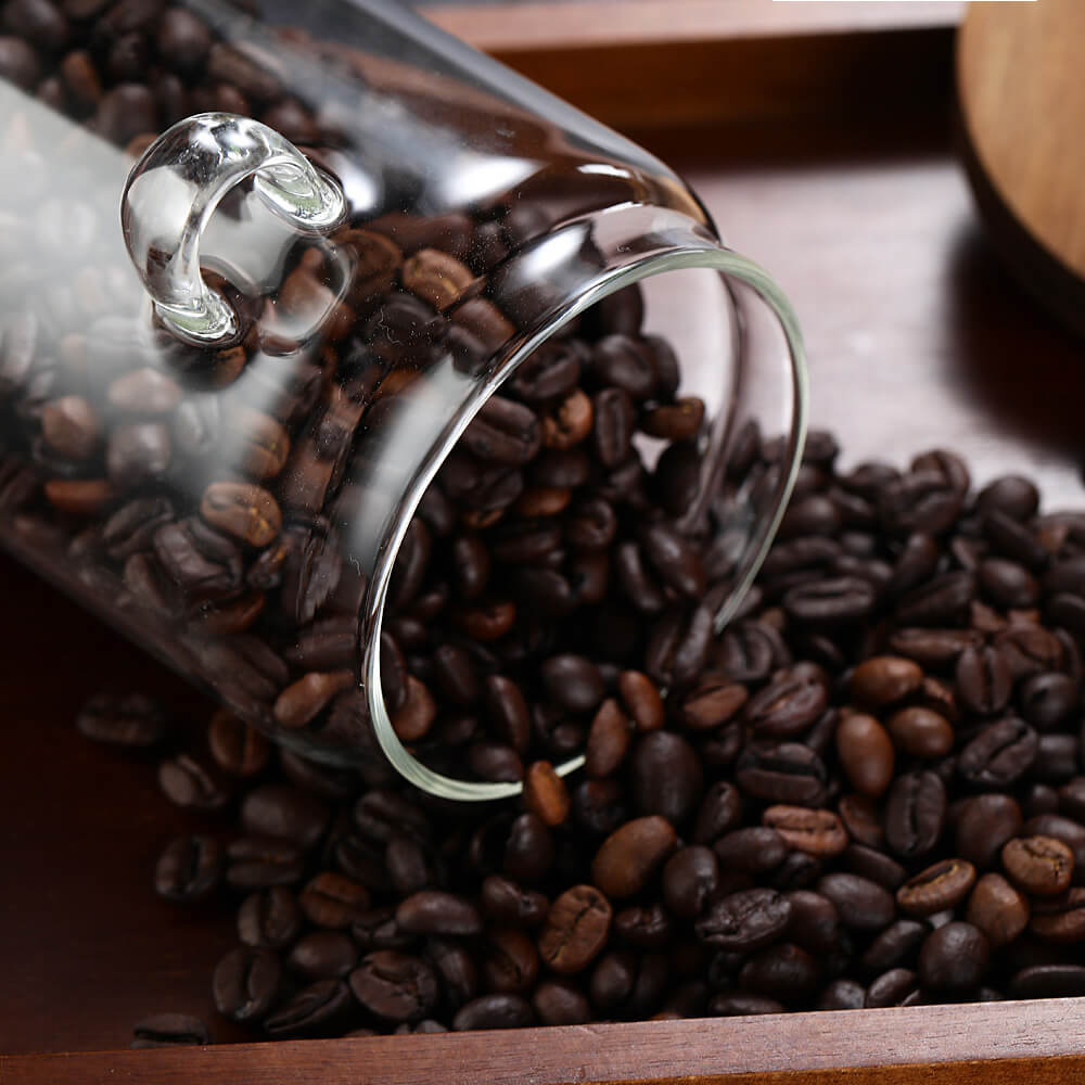 Glass storage jar filled with coffee beans next to wooden spoon on warm surface