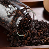 Glass storage jar filled with coffee beans next to wooden spoon on warm surface