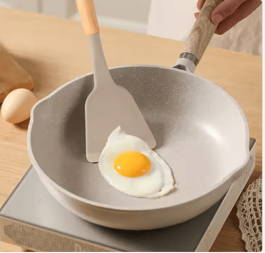 Silicone spatula with wooden handle cooking fried egg in non-stick pan