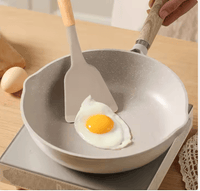 Silicone spatula with wooden handle cooking fried egg in non-stick pan